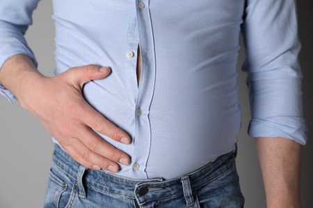 Overweight man in tight shirt on gray background, closeup