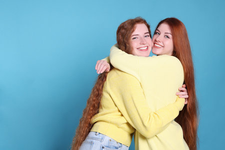 Portrait of beautiful young redhead sisters on light blue background. Space for textの写真素材