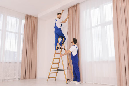 Workers in uniform hanging window curtain indoorsの写真素材