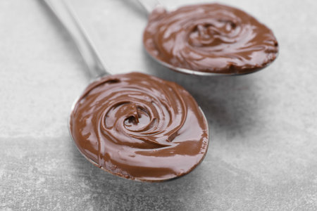 Spoons with chocolate paste on gray textured table, closeup