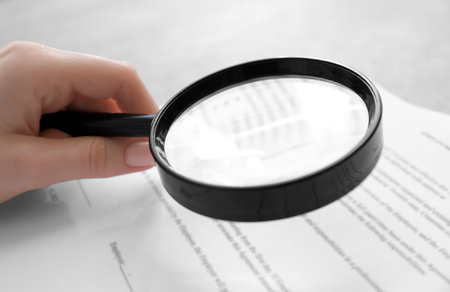 Woman looking at document through magnifier at table, closeup. Search conceptの写真素材