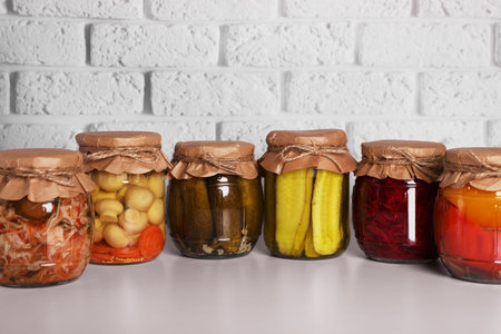 Many glass jars with different preserved vegetables and mushrooms on light gray tableの写真素材