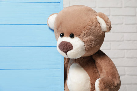 Cute teddy bear near light blue wooden wall against brick background, space for textの写真素材