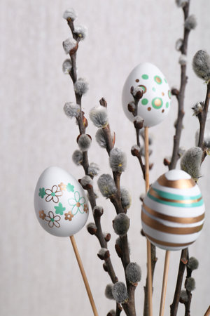 Beautiful willow branches with painted eggs on light gray background, closeup. Easter decor