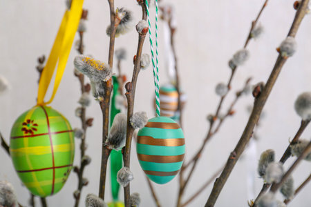 Beautiful willow branches with painted eggs on light blue gray background, closeup. easter decor