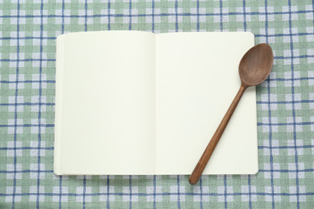 Blank recipe book and wooden spoon on checkered tablecloth, top view. Space for textの写真素材