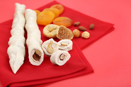 Delicious churchkhelas, nuts and dried fruits on red background, closeup. Space for textの写真素材