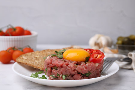 Tasty beef steak tartare served with yolk, pepper, bread and greens on white marble tableの写真素材