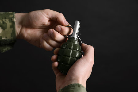 Soldier pulling safety pin out of hand grenade on black background, closeup. Military serviceの写真素材