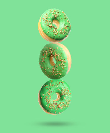 Tasty donuts with sprinkles falling on light green backgroundの写真素材