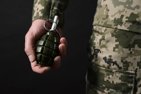 Soldier holding hand grenade on black background, closeup. Military serviceの写真素材