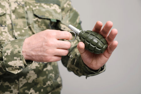 Soldier pulling safety pin out of hand grenade on light gray background, closeup. Military serviceの写真素材