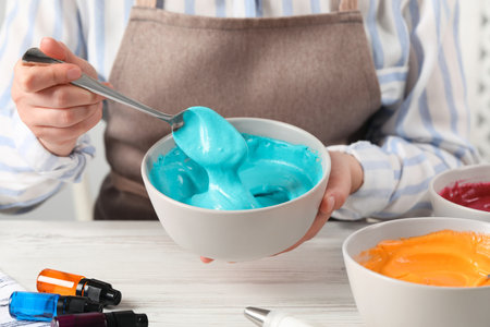 Woman mixing cream with light blue food coloring at white wooden table, closeupの写真素材