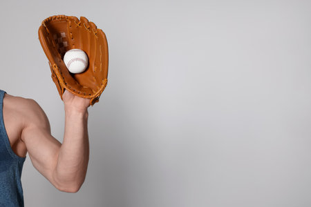 Athletic man with glove and baseball ball on light gray background, closeup. Space for textの写真素材
