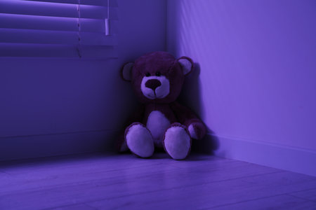 Cute lonely teddy bear on floor in corner of dark roomの写真素材