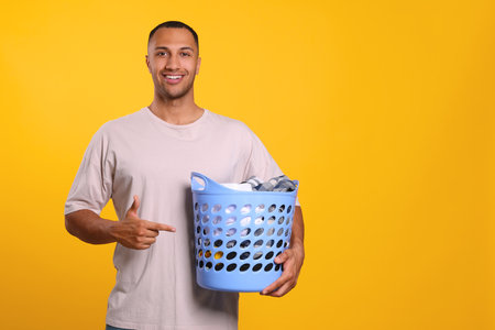 Happy man with basket full of laundry on orange background. Space for textの写真素材