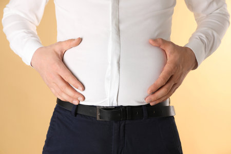 Overweight man in tight shirt on yellow background, closeupの写真素材