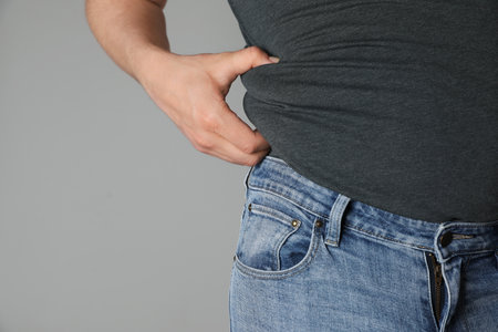 Overweight man in tight tshirt and jeans on light gray background, closeup. Space for textの写真素材