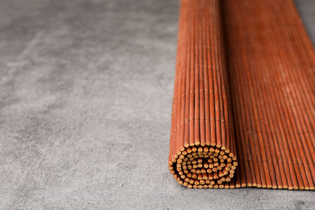 Rolled bamboo mat on gray table, closeup. Space for textの写真素材