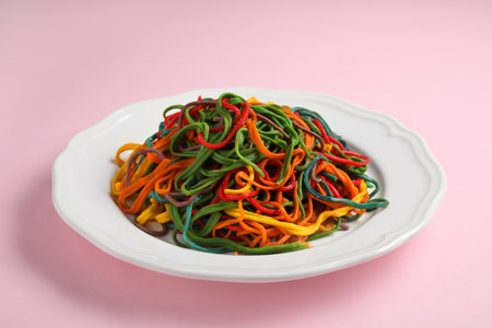 Plate of spaghetti painted with different food colorings on pink backgroundの写真素材