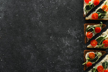 Food photography. Tasty sandwiches with cream cheese, tomato, basil and microgreen on gray textured table, flat lay with space for textの写真素材