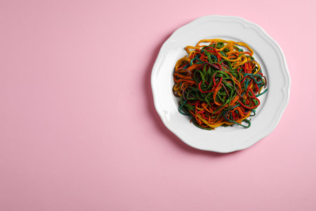 Plate of spaghetti painted with different food colorings on pink background, top view. Space for textの写真素材