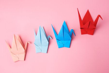Colorful paper origami cranes on pink background, flat layの写真素材
