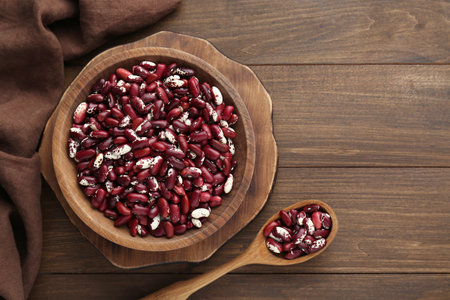 Bowl and spoon with dry kidney beans on wooden table, flat lay. Space for text
