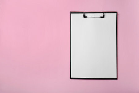 Black clipboard with sheet of blank paper on pink background, top view. Space for textの写真素材