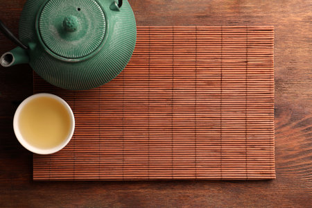 Bamboo mat, teapot and cup of tea on wooden table, top view. Space for text