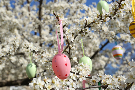 Beautifully painted Easter eggs hanging on blooming cherry tree outdoors