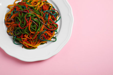 Plate of spaghetti painted with different food colorings on pink background, top view. Space for...