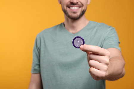 Happy man holding condom on orange background, closeupの写真素材