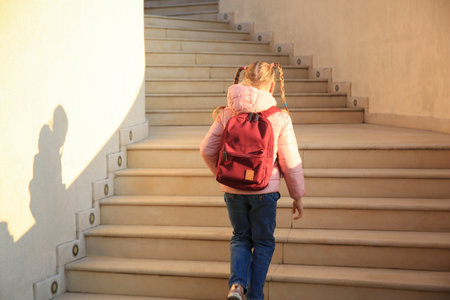 Cute little girl with backpack on stairs outdoors, back viewの写真素材