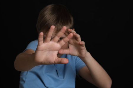 Boy making stop gesture against black background, focus on hands. Children's bullyingの写真素材