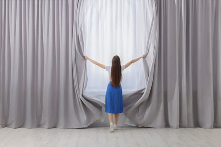 Woman opening stylish curtains at home, back viewの写真素材