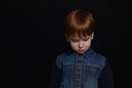 Upset boy on black background, space for text. Children's bullyingの写真素材