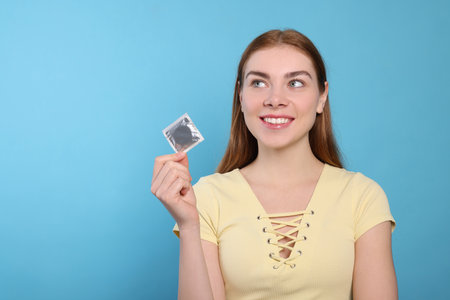 Woman holding condom on turquoise background, space for text. Safe sexの写真素材