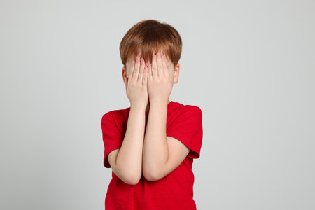 Boy covering face with hands on light gray background. Children's bullyingの写真素材