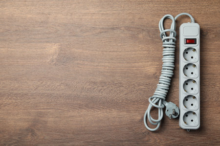 Power strip with extension cord on wooden floor, top view. Space for text