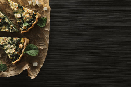 Delicious homemade spinach quiche on black wooden table, top view. Space for textの写真素材