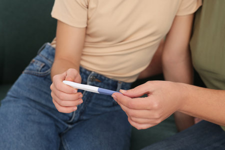 Young woman showing her mother pregnancy test, closeup. Grandparent reaction to future grandsonの写真素材
