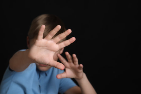 Boy making stop gesture against black background, focus on hands and space for text. Children's bullyingの写真素材