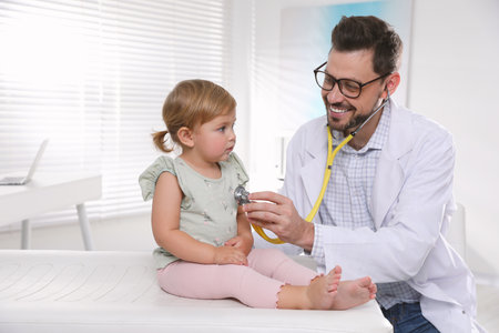 Pediatrician examining baby with stethoscope in clinicの写真素材