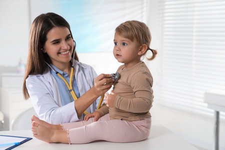 Pediatrician examining baby with stethoscope in clinicの写真素材