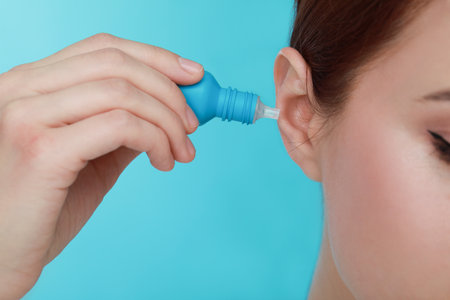 Woman using ear drops on light blue background, closeupの写真素材