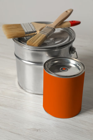 Can of orange paint, bucket and brushes on white wooden tableの写真素材