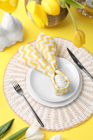 Festive table setting with painted eggs, plates and tulips. Easter celebration