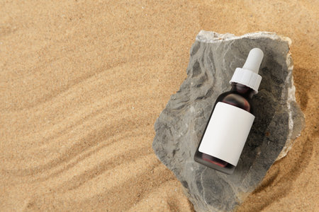 Bottle of serum and stone on sand, top view. Space for textの写真素材