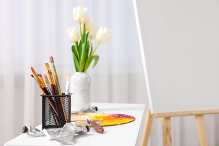 Wooden easel with canvas and art supplies on table indoors. Space for textの写真素材